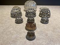 Front view of all flower frogs arranged on a flat surface showing metal cage, metal pin, and glass types