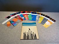Photo of full set of 10 numbered colorful booklets arranged in a semi-circle with portfolio folder in front on gray surface