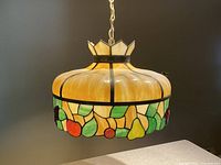 Full view of the stained glass swag chandelier hanging from a chain, showing the top crown and the decorated bottom edge with fruit motif.