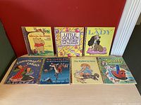 Photo showing seven Little Golden Books arranged in two rows against a red wall. Titles include Winnie the Pooh and Tigger, Little Golden Picture Dictionary, Walt Disney's Lady, Christmas Carols, Rudolph the Red-Nosed Reindeer, The Rabbit is Next, and Scuffy the Tugboat.