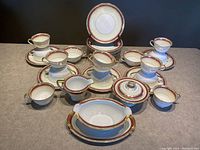 Front view of 34-piece Noritake Elberon China set with teacups, saucers, dessert plates, gravy boat, sugar bowl with lid, and creamer arranged on a table.