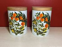 Front view of two ceramic jars with colorful lemon and orange artwork and wooden lids on top