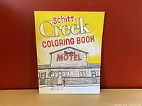 Front cover of the Schitt's Creek Coloring Book with Rosebud Motel illustration.