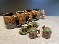 Four vintage Shafford ceramic mugs shaped like tree stumps with beaver handles, accompanied by matching salt and pepper shakers and a tray, all with Canadian maple leaf decorations.