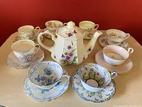 Full view of all tea set items including teapot and eight floral teacups with saucers