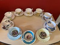 Top-down view of all ten sets of floral teacups and saucers arranged around a wooden table.