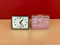 Two vintage electric alarm clocks side by side, brown Minikin and pink Westclox Sizzler.