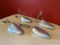Two pairs of vintage aluminum shoe stretchers displayed on a wooden surface with red background.