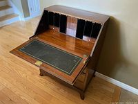 Open view of the vintage wooden bureau writing desk with the drop front writing surface lowered, showing the black secretary compartments and small drawers inside.