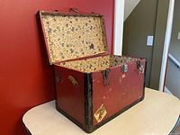 Open vintage wooden toy chest showing red exterior and decorative interior lining with children's motifs.