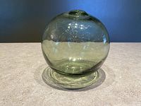Front and side view of the green glass fishing float showing spherical shape, thick glass, and sealed top opening.