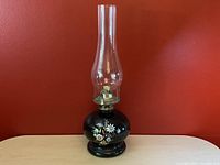 Full view of vintage oil lamp showing black ceramic base with floral design and tall clear glass chimney