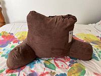 Front view of the brown faux suede back rest pillow set on a colorful bedspread, showing its backrest and armrests.