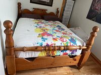 Full view of vintage wooden four-poster bed with floral bedding in a corner room, showing headboard and posts with round finials.