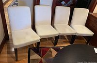 Four IKEA Hendriksdal dining chairs placed in a row, showing wood legs and cream fabric upholstery with some fabric spots.