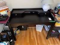 Black wooden desk with two small lockable drawers and raised ledge back panel, photographed from above and front angles showing drawers, finish, and legs.