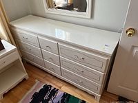 Front view of vintage white dresser with nine drawers and carved drawer fronts, showing overall structure and paint finish.