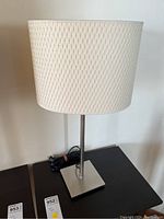 Full view of the table lamp showing the white woven fabric shade and metal base on a dark surface.