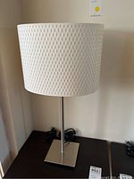 Full view of the table lamp showing the white textured woven fabric shade and metal base.