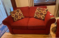 Front view of red fabric loveseat with two decorative cushions