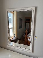 Front view of rectangular mirror showing off-white painted wood frame with scalloped edges and visible finish flaws.