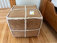 Front view of the tan faux shearling ottoman showing the grid pattern and texture of the fabric.