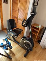 Side view of the bike showing seat, backrest, arm handles, pedals and front digital display console.