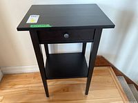 Front view of the black wooden side table showing the drawer and lower shelf