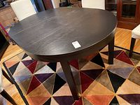 Angled view showing the dark wood veneer round dining table surface with visible wear and mostly extended leaf installed