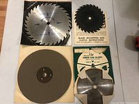 Overview photo showing all five items - one 10 inch chrome-plated calibration plate, one sanding disk, and three saw blades along with mounting and clutch instructions included.