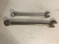 Top view of two metal wrenches side by side on white surface, one is longer and heavier, both have open and box ends.