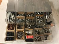 Top view of two plastic storage units side by side, each with five translucent pull-out drawers containing assorted metal hardware including screws, bolts, washers, nuts, nails, metal hooks and fasteners.