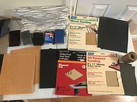 Top-down photo showing assorted sandpaper sheets, sanding sponge, and rolled sandpaper sheet on a white surface.