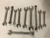 Nine assorted wrenches including combination and open-end types laid out on white surface.