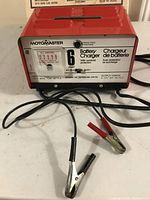 Front view of Motomaster battery charger with clamps laid out on white surface.