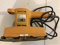 Top angle of orange Black & Decker sheet sander showing sanding base and front label.