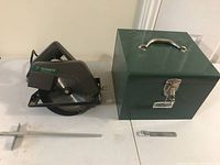 View of circular saw, metal case, guide bar, and metal lever arranged on white surface.