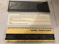 Yellow CN Rail metric conversion rule with black sliding bar and measurement scales, placed on a white surface alongside instruction sheet and black pouch.