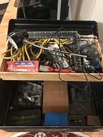 Top view of open metal tool box with removable tray containing lamp, extension cord, clamps, ruler, screwdriver, and small hardware items