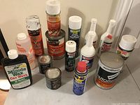 Photo showing various automotive liquids and spray cans on table displaying labels and variety of product types.