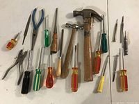 Top view of a assortment of hand tools including hammers, screwdrivers, pliers, and files arranged on a white surface.