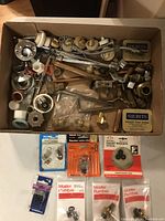 Box lot containing a variety of plumbing parts including metal and plastic fittings, tubes, washers, and vintage collectible tins.