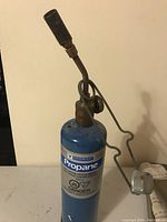 Front view of the propane hand torch with blue propane tank, showing the propane brand and danger warning labels.