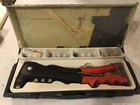 Riveter tool in molded plastic case showing tool and compartments for rivet heads.