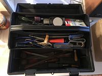 View of opened tool box showing top removable tray filled with various hand tools, pliers, screwdrivers, hacksaw blade, small mirror, and other items.