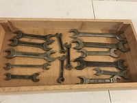 Photo of multiple vintage British spanner wrenches arranged inside a wooden tray, showing their overall condition and layout.