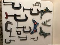 Overhead view of all clamps laid out on white tabletop showing diverse sizes, colors, and styles including corner clamps and C-clamps.