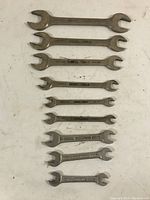 Top-down view of set of 8 vintage open-ended wrenches arranged in descending size order on a white surface