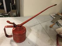 Red metal vintage oil dispenser with a long spout and handle shown from front angle.