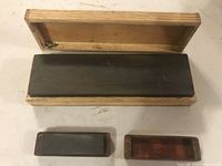 Open wooden box showing the large sharpening stone inside and the smaller stone placed outside the box for scale.